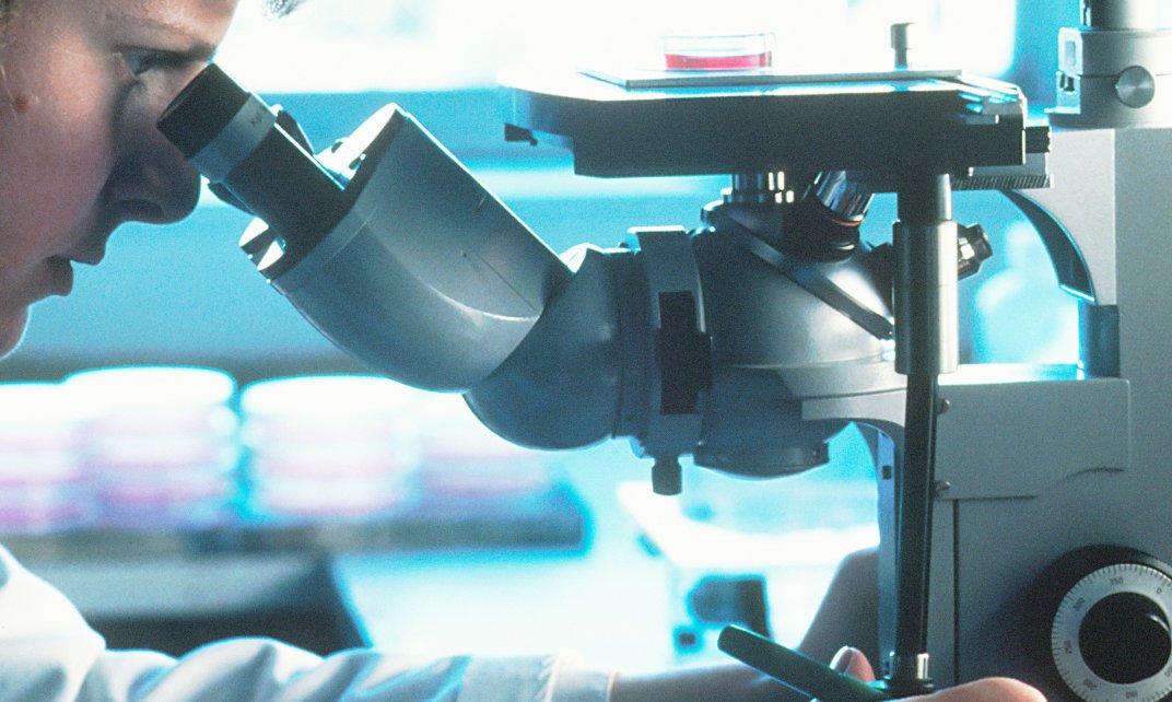 Een vrouwelijke wetenschapper werkt met een microscoop. 